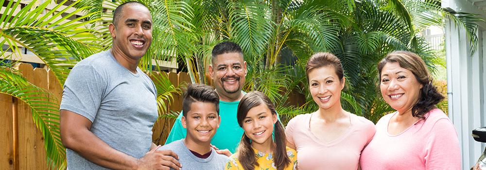 A Hawaiian family with healthy teeth smiles while enjoying a celebration in their yard. 