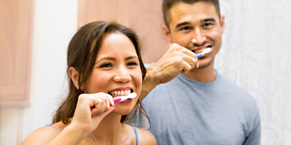 A Hawaiian man and woman are happily brushing their teeth.