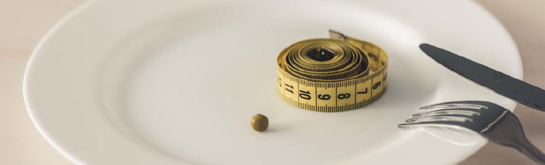 A roll of measuring tape and a small pea are on a dinner plate to show how eating disorders can distort the perception of food